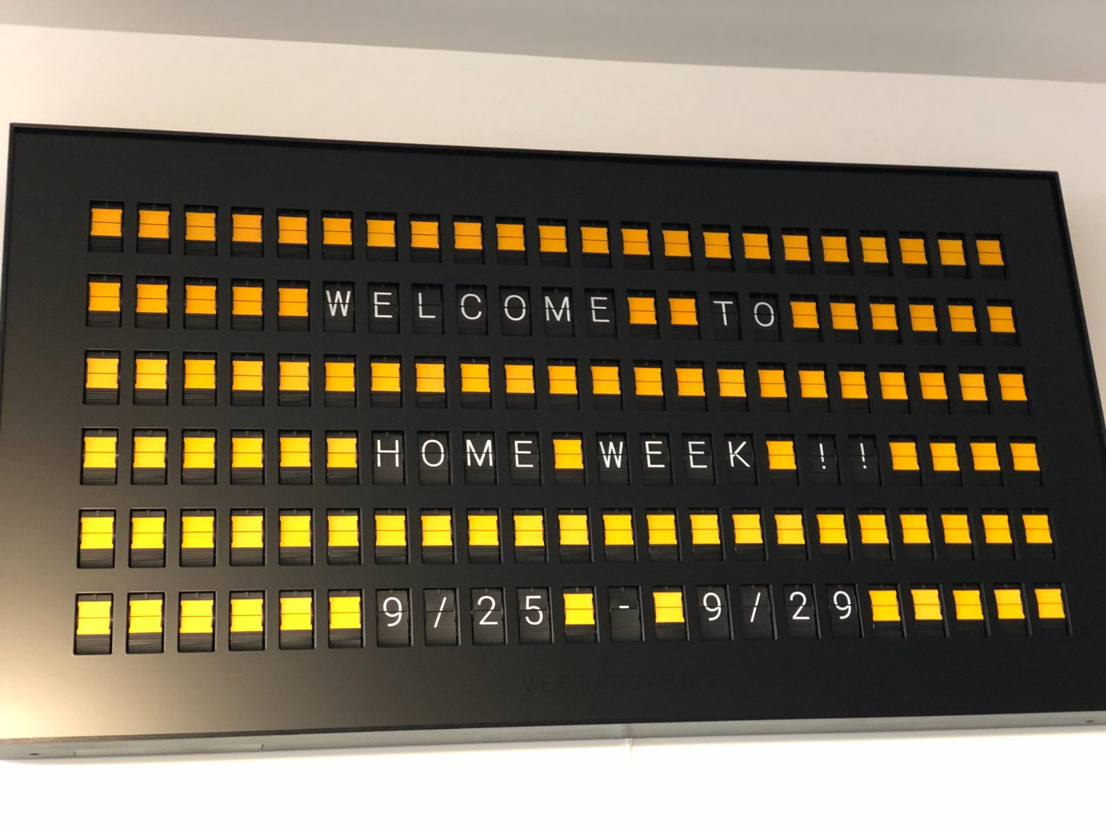 A flip-dot sign in the studio reading Welcome to Home Week