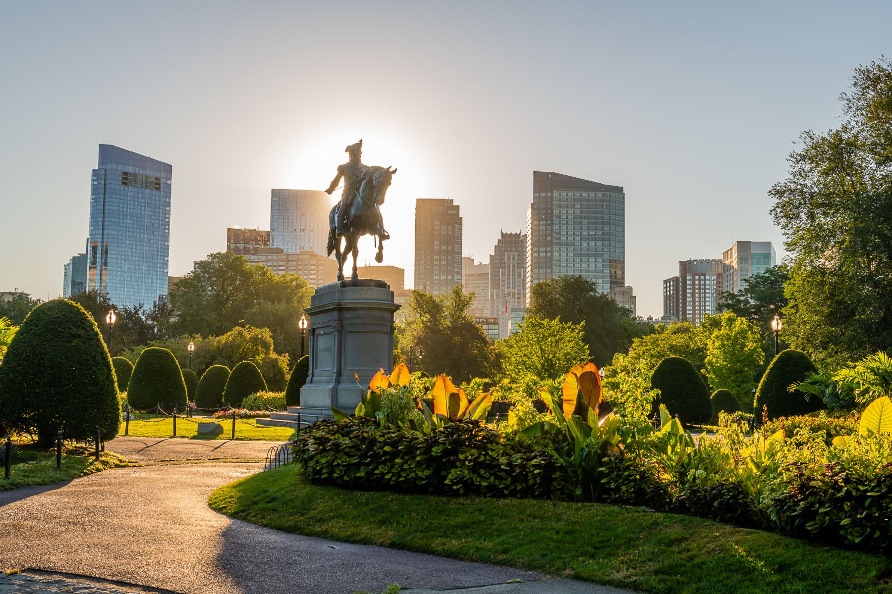 The Boston skyline at sunrise seen from the Public Garden, behind the George Washington equestrian statue.