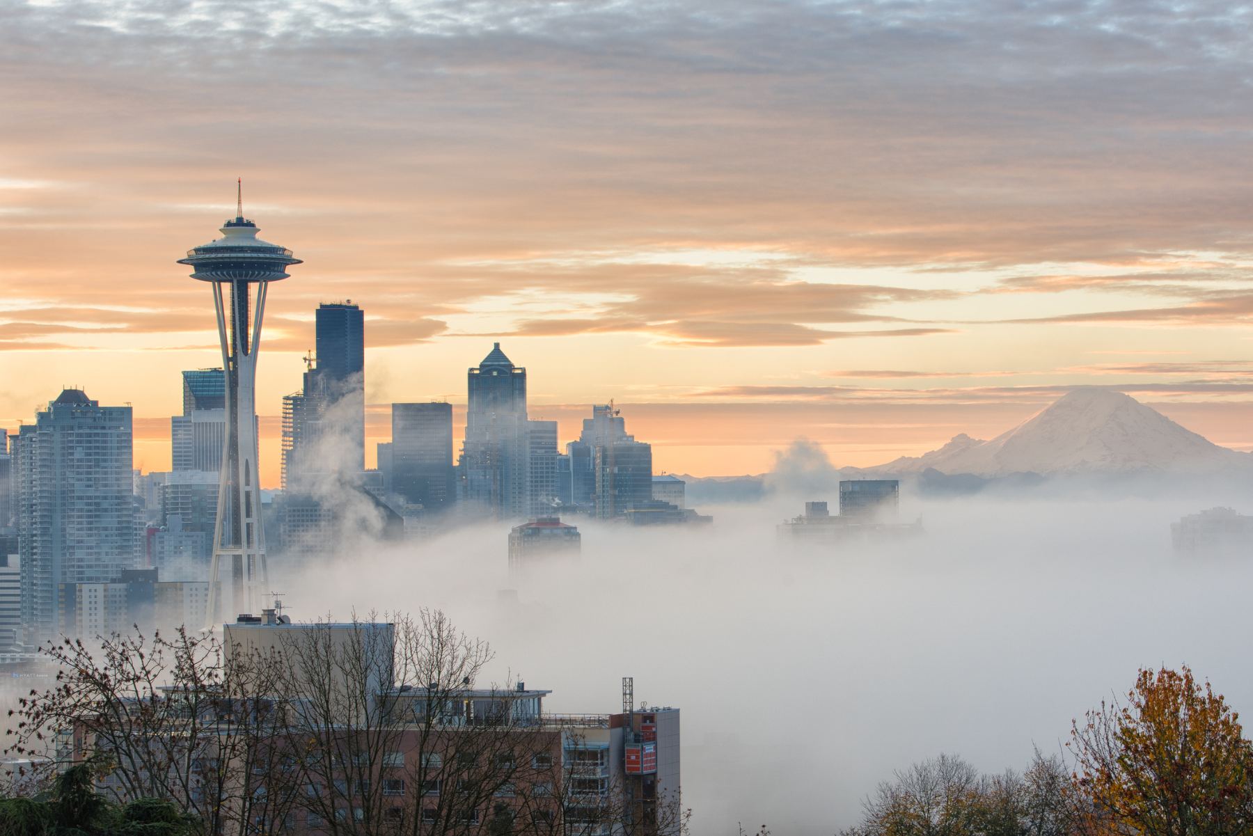 The Seattle skyline at sunrise, the Space Needle above low fog with Mount Rainier on the horizon.